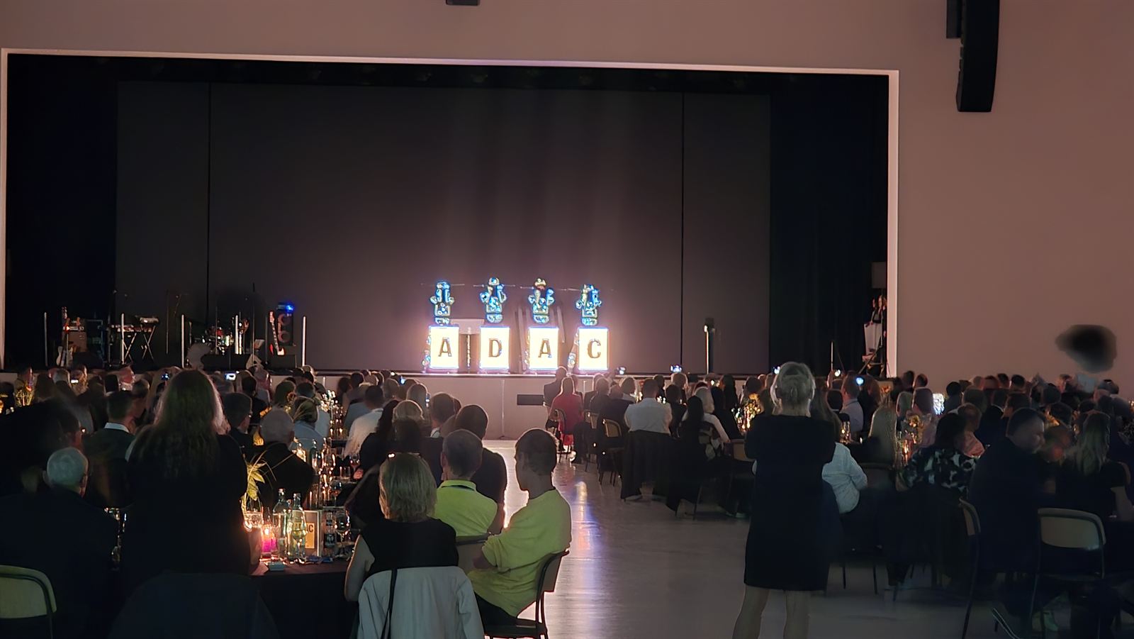 Leuchtende ADAC-Buchstaben auf einer Bühne vor Publikum an Dinner-Tischen
